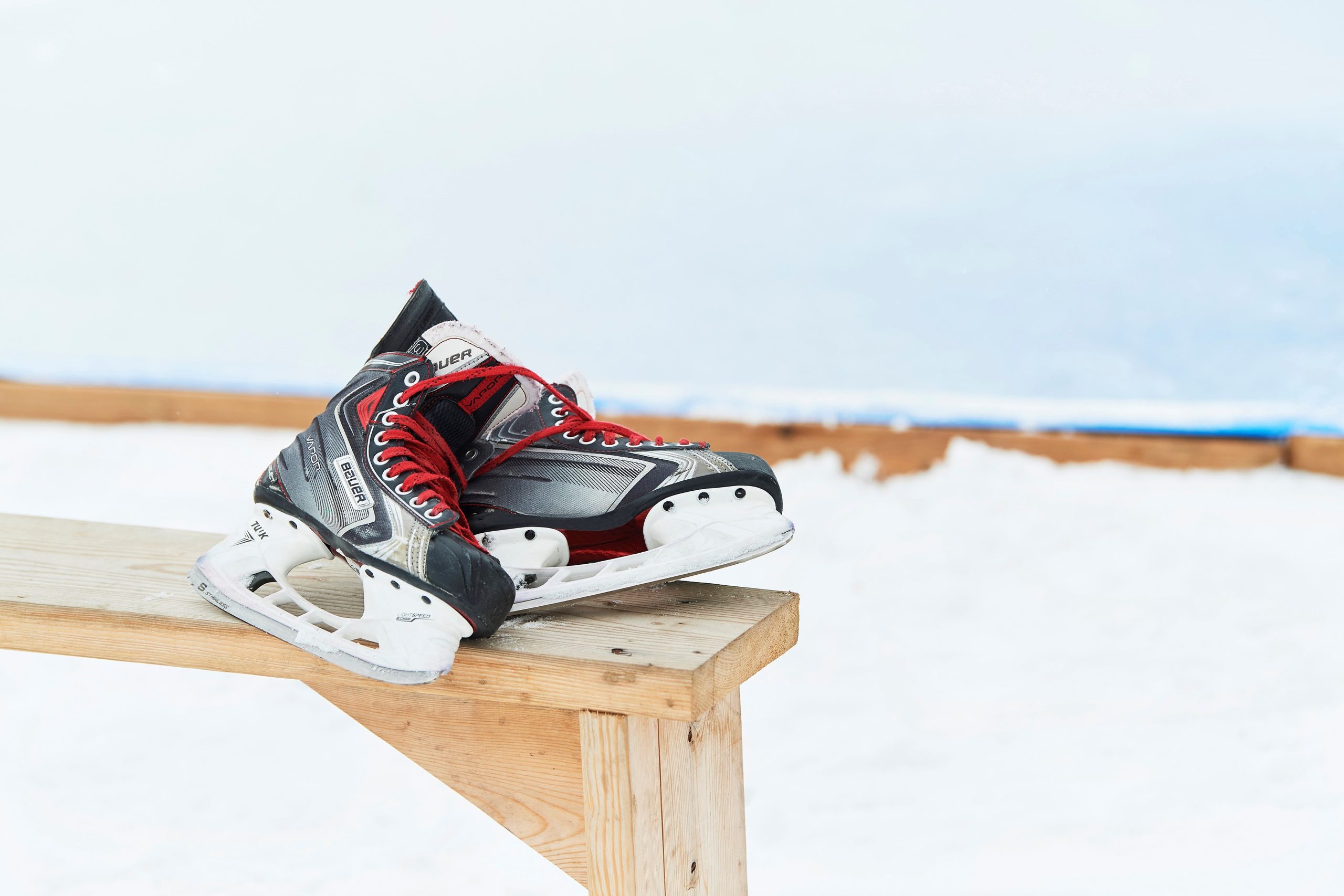 Ice skates sit atop a wooden bench beside the ice rink.