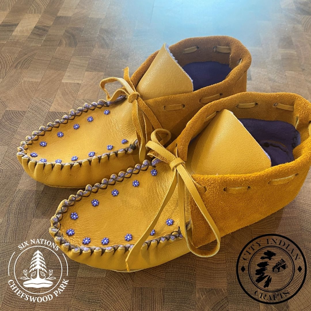 Women's moccasins with purple beaded flowers around the toes.